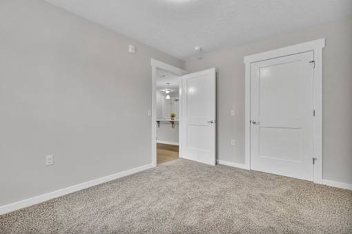 A room with white walls and a carpeted floor with two white doors.