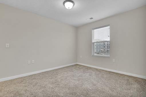 A room with a carpeted floor and a window with blinds.