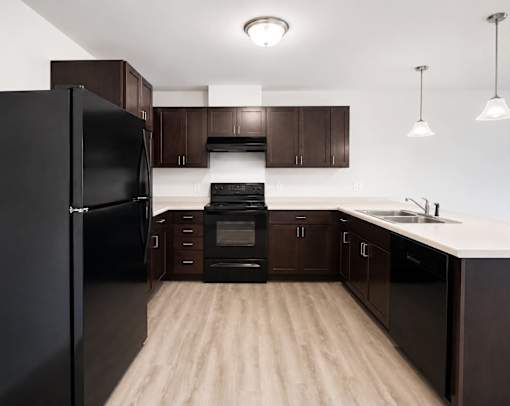 A black refrigerator stands in a kitchen with wooden floors and brown cabinets.