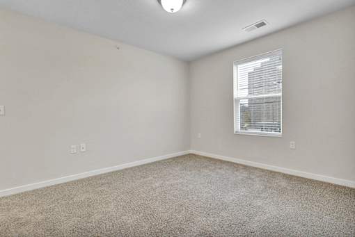 A room with a carpeted floor and a window with blinds.