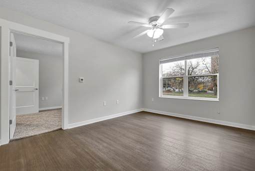 A room with a ceiling fan and a window with a view of trees.