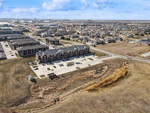 A large open field with a building complex in the middle and a residential area in the background.