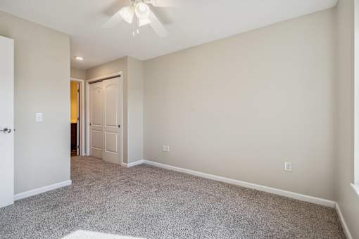 A room with a carpeted floor and a ceiling fan.