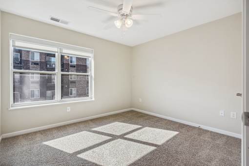 A room with a ceiling fan and a window overlooking a building.