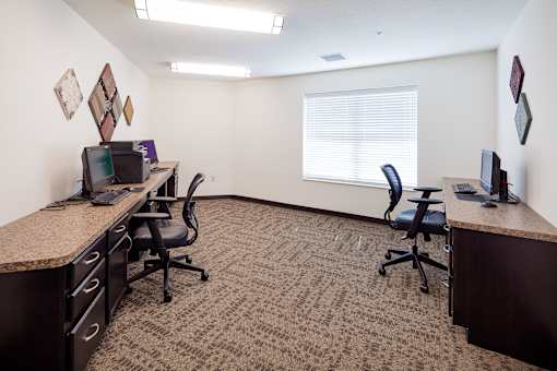 A carpeted office room with two desks and chairs.