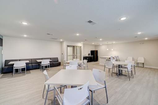A white table surrounded by white chairs in a room with a black sofa.