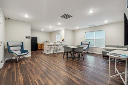 A room with a wooden floor and white walls has a table and chairs.
