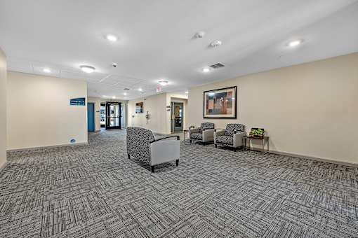 A hallway with a carpeted floor and a few chairs and a table.
