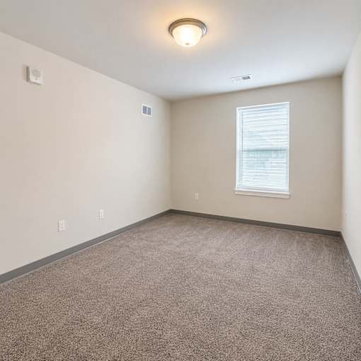 A room with a window and a smoke detector on the wall.