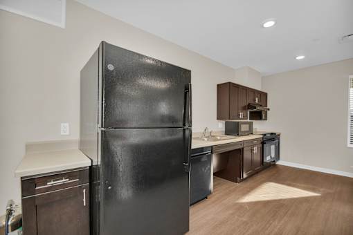 A black refrigerator stands in a kitchen with wooden floors and brown cabinets.