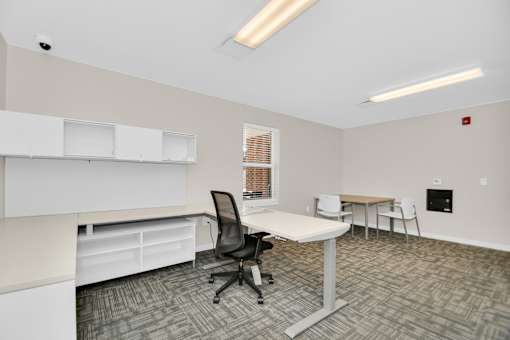 A room with a desk, chairs, and a window with blinds.
