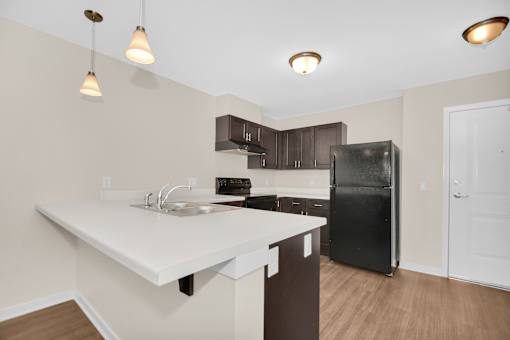 A kitchen with a black refrigerator and brown cabinets.