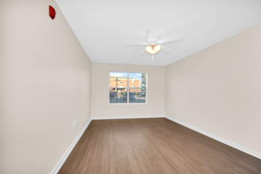 A room with a ceiling fan and a window showing a building outside.