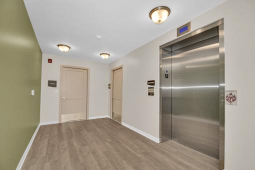 A hallway with a stainless steel elevator on the right and two doors on the left.