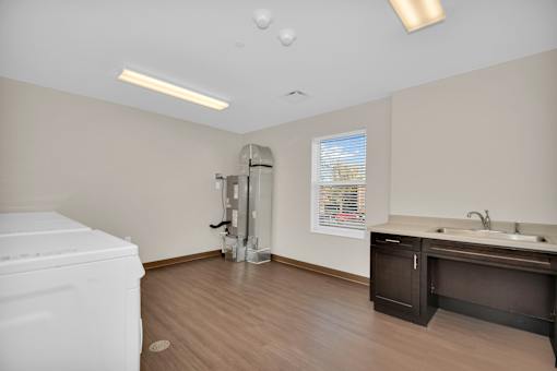 A white washing machine sits in a small laundry room with a sink and a window.