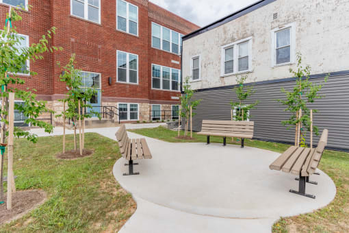 a courtyard with benches and trees in front of a brick building