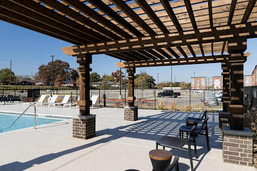 A wooden pergola over a pool with lounge chairs underneath.