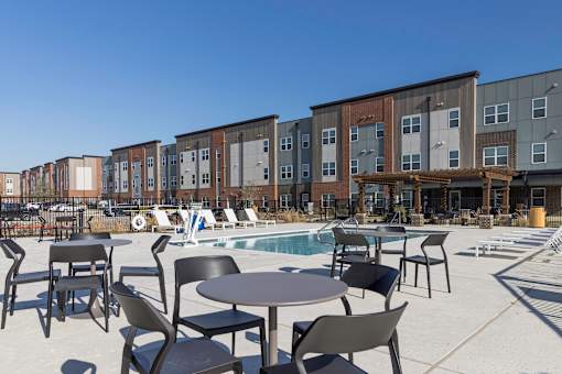 A pool area with chairs and tables in front of apartment buildings.