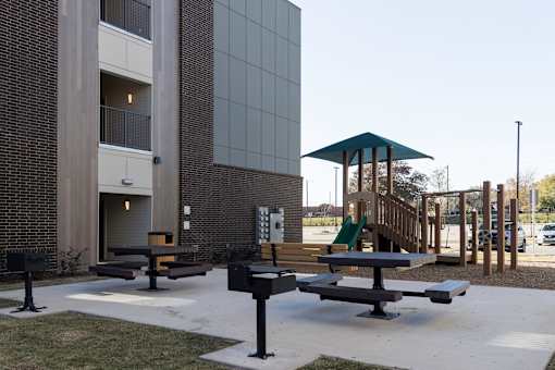 A playground area with a slide and picnic tables in front of a building.
