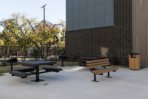 A black picnic table and bench in front of a brick building.