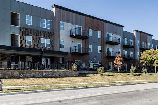 Apartment building with balconies and a stone wall in front.