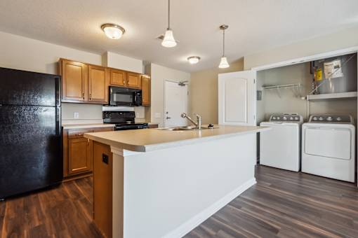 A kitchen with a black refrigerator, white countertops, and wooden cabinets.