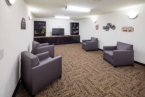A room with brown carpet and grey chairs.
