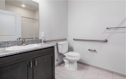 A white toilet sits in a bathroom next to a sink and a towel bar.