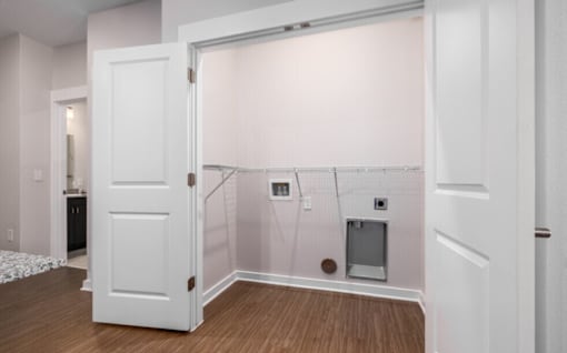 A white door is open to a room with a white wall and a brown floor.