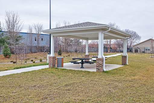 A white pavilion with a brick pillar stands in a grassy field.