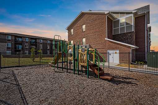 A playground with a slide and a green fence in front of a brick building.