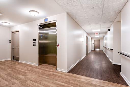 A long hallway with a wooden floor and a metal elevator.