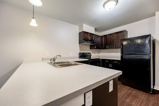 A kitchen with a black refrigerator and brown cabinets.