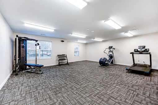 A spacious gym with a variety of equipment including a treadmill, a weight bench, a rowing machine, and a stationary bike.