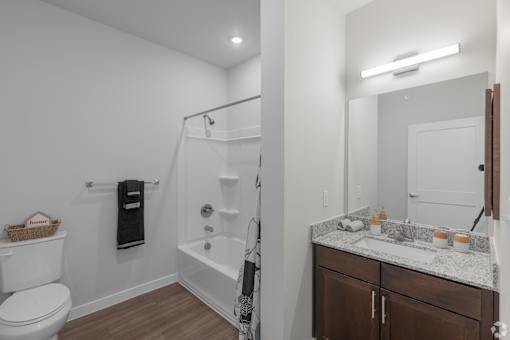 A white toilet is in a bathroom with a white tub and a brown cabinet.
