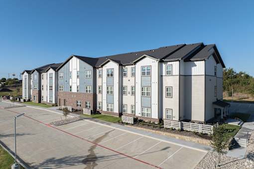 A row of modern townhouses with a parking lot in front.