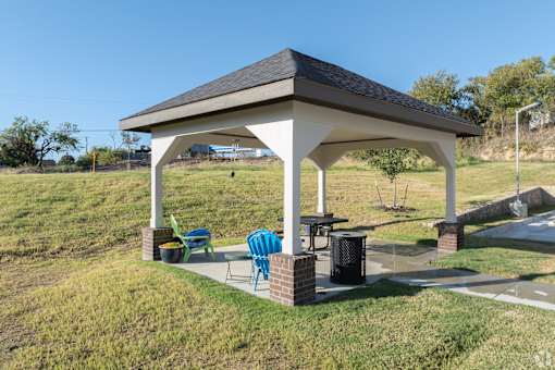 A white gazebo with a black roof is surrounded by green lawn chairs and a brick pillar.