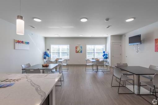 A spacious room with tables and chairs is well lit with ceiling lights.