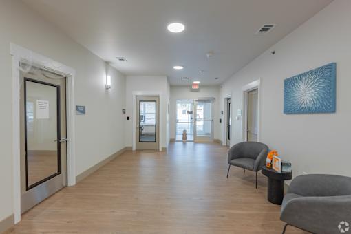A hallway with a blue artwork on the wall and two grey chairs on the right side.