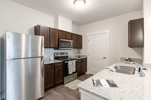 A kitchen with a refrigerator, microwave, oven, sink, and cabinets.