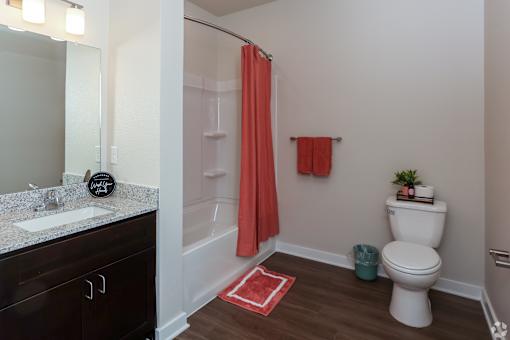 A bathroom with a white toilet, a red rug, and a red shower curtain.