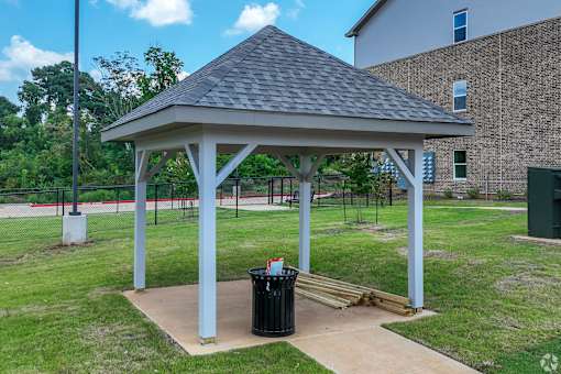 A gazebo is surrounded by a grassy area and a brick building.