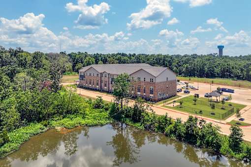 A large building sits in the middle of a green field with a water body in front of it.
