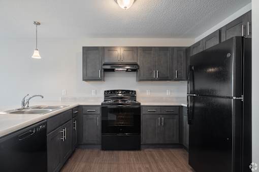 A black fridge in a kitchen with wooden floors and black cabinets.