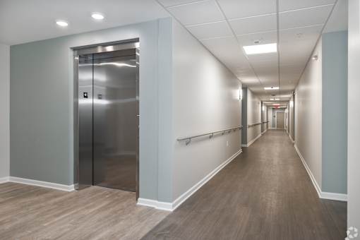 A long hallway with a silver elevator on the left.