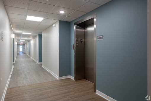 A long hallway with a silver elevator on the right.
