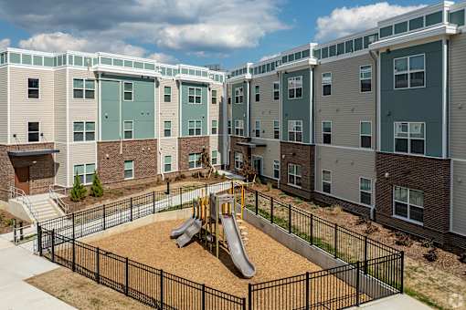 A playground area with a slide and sandbox in front of apartment buildings.