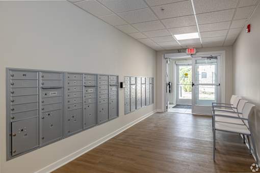 A hallway with a row of mailboxes on the wall and a bench on the right.