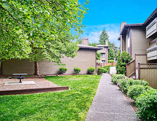 A backyard with a picnic table and a concrete path at apartments in Renton, WA.