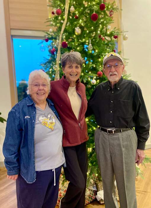 Three people pose in front of a Christmas tree at Hearthstone Lodge Senior Residences, California